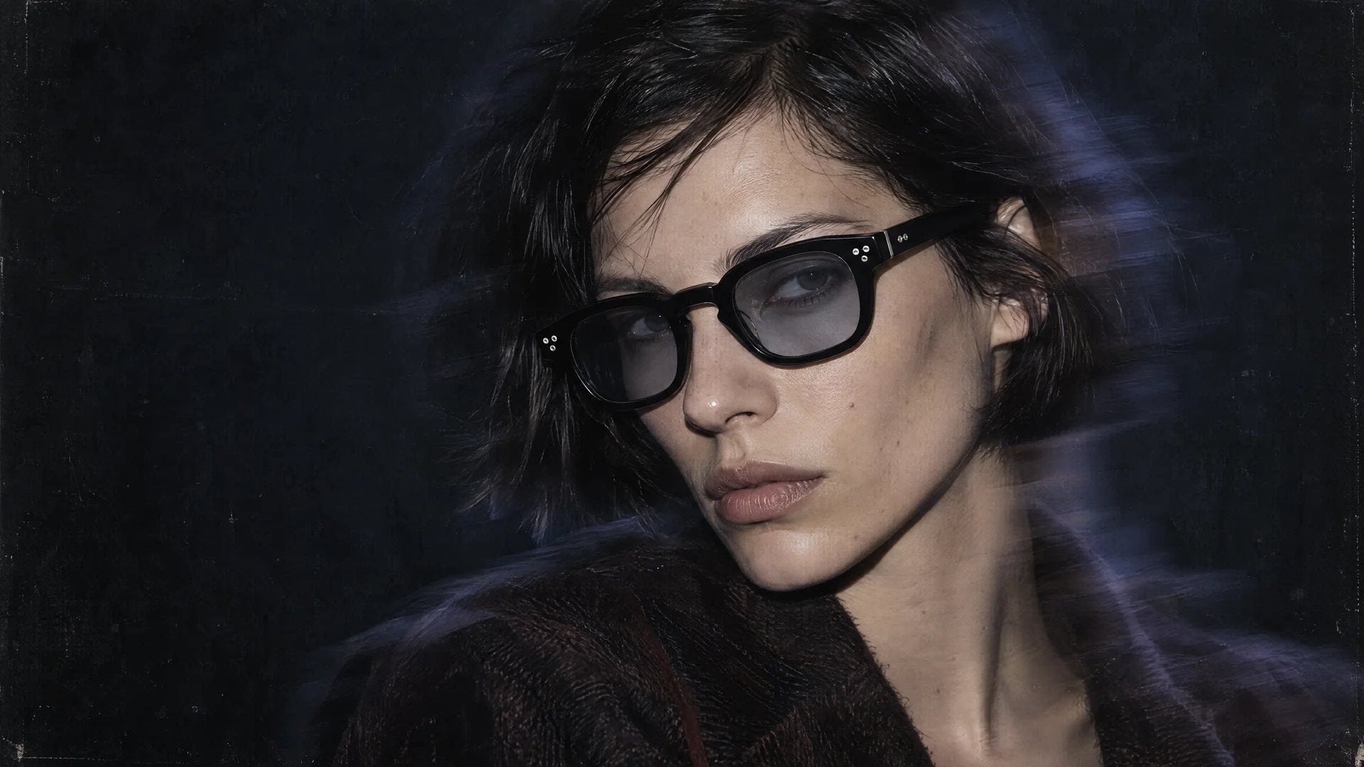 Woman with short dark hair wearing black Nano frames with rivets and blue-tinted lenses